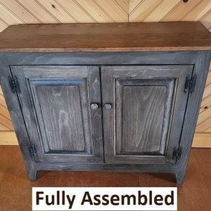 May include: A dark gray wooden cabinet with two doors and a wood top. The cabinet has black hinges and knobs. The cabinet is fully assembled. "Fully Assembled" is written in black text at the bottom of the image.