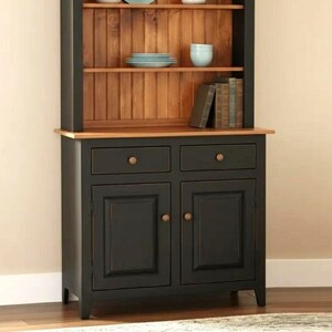May include: A black and walnut hutch featuring two lower cabinet doors, two drawers with round knobs, and two open shelves with a vertical plank back. The unit displays plates, bowls, and books. The text Black + Walnut is visible below.