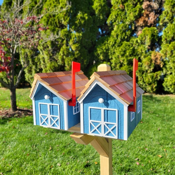Peut inclure: Une boîte aux lettres en bois bleue et brune avec deux compartiments séparés. Chaque compartiment a un drapeau rouge sur le dessus. La boîte aux lettres est montée sur un poteau en bois.