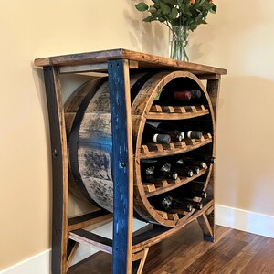 May include: A reclaimed barrel wine rack with a wooden top and base. The rack incorporates a section of the barrel to hold wine bottles. The frame is stained in dark colours. A vase of orange roses sits on top of the rack.