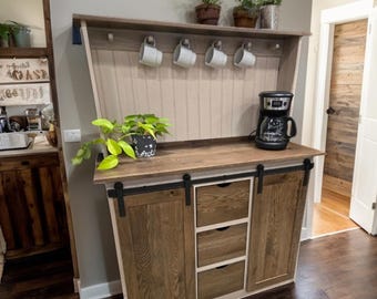 May include: A white and brown wooden coffee station with a sliding door cabinet, three drawers, and a top shelf with hooks for mugs. The coffee station has a black countertop and a coffee maker on the counter. The text "Fully Assembled" is visible at the bottom of the image.