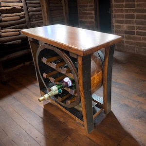 May include: A wooden wine rack and table. The table has a rectangular top and is supported by a frame that incorporates a section of a wine barrel. The rack holds several wine bottles. The table is approximately 76 cm long.