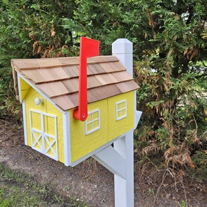 May include: A whimsical yellow mailbox with a cedar shake roof and a bright red flag. The mailbox has white trim and two small windows. The design resembles a miniature house, mounted on a white post.