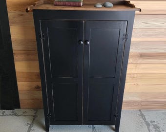 May include: A black wooden cabinet with two doors and a wooden top. The cabinet has a simple design with two round knobs and visible hinges. The top of the cabinet holds a stack of books and two small stones. The text "Fully Assembled" is at the bottom.