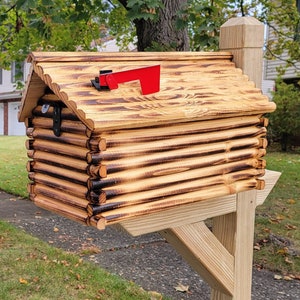 May include: A wooden mailbox shaped like a log cabin with a red metal flag. The mailbox is mounted on a wooden post.