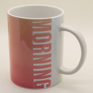 K&ouml;nnte beinhalten: Wei&szlig;e Keramiktasse mit einem Ombre-Design von Rosa zu Orange und dem Wort "MORNING" in Wei&szlig; auf der Seite.