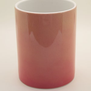 K&ouml;nnte beinhalten: Eine Keramiktasse mit einem Ombre-Design von Pink zu Wei&szlig;. Die Tasse ist leer und hat eine glatte, gl&auml;nzende Oberfl&auml;che.