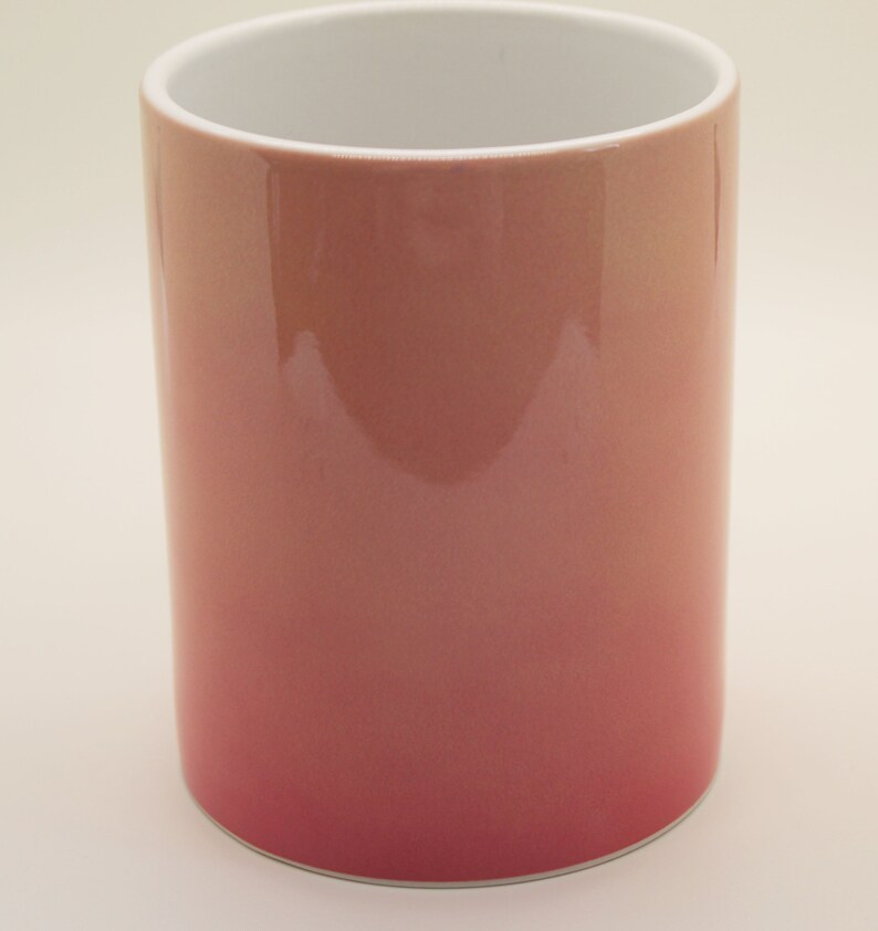 K&ouml;nnte beinhalten: Eine Keramiktasse mit einem Ombre-Design von Pink zu Wei&szlig;. Die Tasse ist leer und hat eine glatte, gl&auml;nzende Oberfl&auml;che.