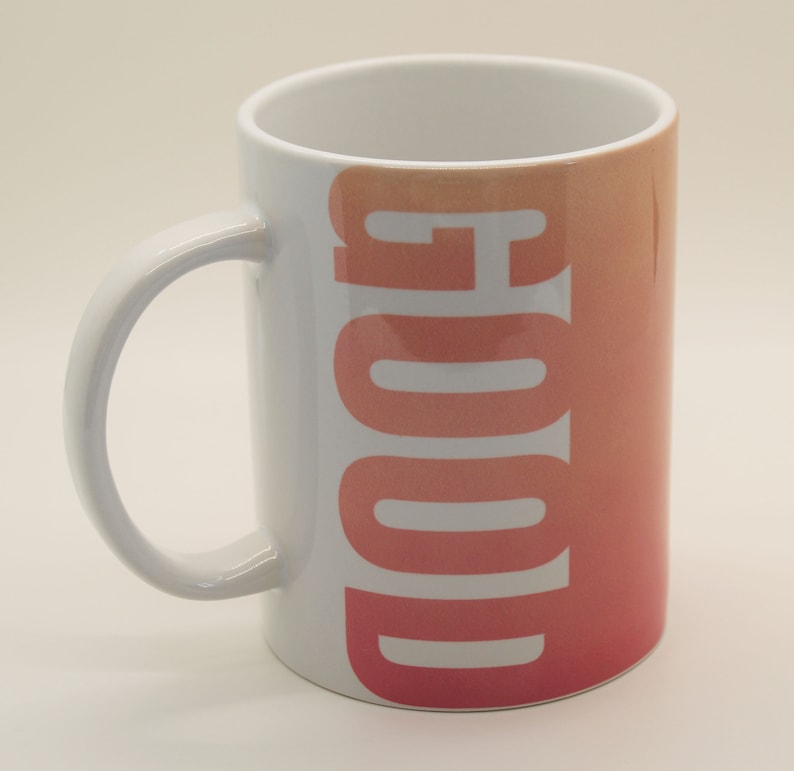 K&ouml;nnte beinhalten: Wei&szlig;e Keramiktasse mit einem rosa-orangenen Farbverlauf und dem Wort "GOOD" in wei&szlig; auf der Vorderseite.