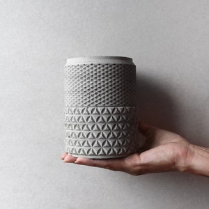 May include: A gray concrete planter with a geometric pattern. The planter is made of two sections, each with a different pattern.