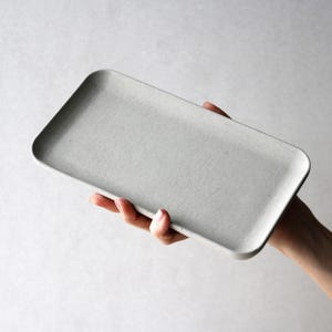 以下が含まれることがあります： わずかにテクスチャ加工された表面を持つ、長方形の薄い灰色のセラミックトレイ