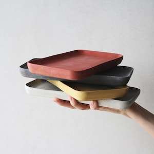 以下が含まれることがあります： 4つの長方形のトレイが積み重ねられています。一番上のトレイは赤、2番目のトレイはグレー、3番目のトレイは黄色、一番下のトレイは白です。