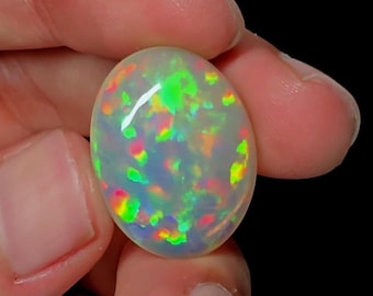 May include: A white opal cabochon with a rainbow of colors, including green, red, and blue.