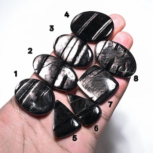 May include: Eight polished black obsidian cabochons with silver sheen, numbered 1 through 8. Each stone features distinct carved grooves across its surface, displaying a reflective metallic luster against the dark, smooth, and rounded gemstone material.