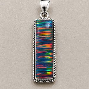 Peut inclure: Un pendentif rectangulaire doté d'une incrustation d'opale multicolore vibrante avec des stries horizontales bleues, vertes, orange et rouges. La pierre est sertie dans un cadre en argent poli avec une bordure en corde torsadée et une bélière.
