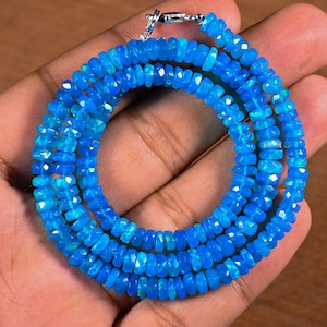 May include: A necklace composed of small, faceted, vibrant blue opal beads arranged in a circular pattern. The strand features a polished silver-toned metal lobster claw clasp at the top, securing the continuous loop of bright, reflective gemstone beads.