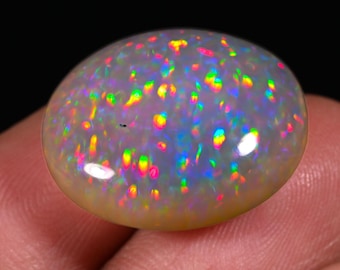 May include: A white opal cabochon with a rainbow of colors, including red, orange, yellow, green, blue, and purple. The opal has a speckled pattern and is set in a silver ring.
