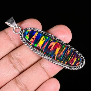 May include: An elongated oval pendant featuring a dark, iridescent opal with vibrant flashes of red, green, and yellow color play. The gemstone is set in a polished silver frame with a twisted rope texture and includes a triangular silver bail.