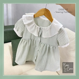 May include: A green and white striped dress with a white Peter Pan collar and short sleeves. The dress has a button closure and a gathered skirt. The dress is labeled "DRBB-07 - Sewing Pattern -" and "Baba Corner Made with love".