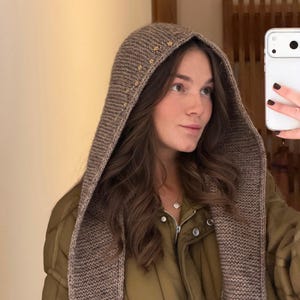 Może przedstawiać: Brązowy dzianinowy kaptur z małymi złotymi zdobieniami. Kaptur jest noszony na zielonej kurtce. Kaptur to stylowy dodatek na chłodne dni. Kaptur jest wykonany z miękkiego, ciepłego materiału.