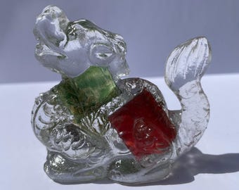 May include: A clear glass figurine of a mythical creature, possibly a dragon or sea serpent. The figure has a green section at the neck and a red section on its body. The details of the figure are visible through the clear glass.