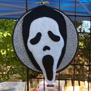 May include: A white felt ghost mask with black eyes and a black open mouth, sewn onto a gray and white fabric circle.
