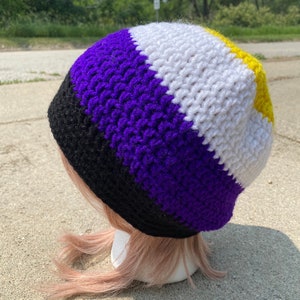 May include: A crocheted beanie hat with black, purple, white, and yellow stripes. The hat is made with a textured stitch.
