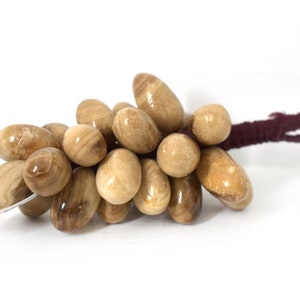 以下が含まれることがあります： 濃い茶色の紐で結ばれた、滑らかで明るい茶色の石の塊。石はブドウのような形に配置されています。