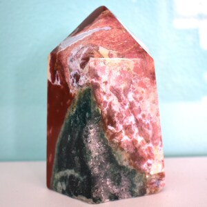 Puede incluir: Una gran punta de cristal multicolor con tonos de rojo, rosa, blanco y verde. El cristal está pulido y tiene una superficie lisa y brillante.