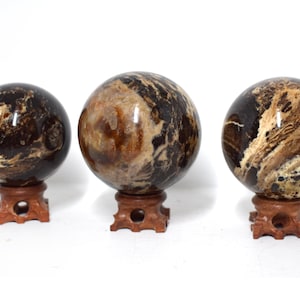 Puede incluir: Tres esferas de ágata pulidas de color marrón y blanco sobre soportes de madera. Las esferas tienen un patrón de remolino de marrón y blanco.