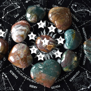 Puede incluir: Diez piedras en forma de corazón, cada una con un patrón único de marrón, verde y blanco, dispuestas en círculo sobre un fondo negro con símbolos del zodíaco.