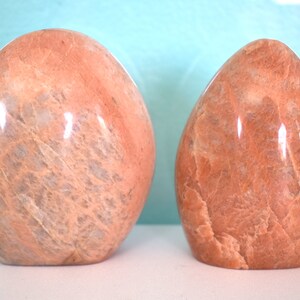Puede incluir: Dos piedras lisas y pulidas de forma ovalada. Las piedras son de color naranja claro con vetas y remolinos blancos.