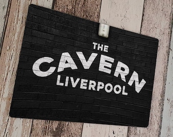 Puede incluir: Señal de pared de ladrillo negro con texto blanco que dice "The Cavern Liverpool".