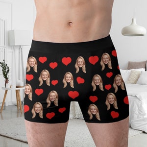 May include: Black boxer shorts with a repeating pattern of red hearts and a woman's face.