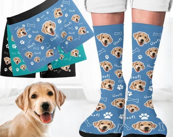 May include: A set of blue socks and boxer shorts with a repeated pattern of a dog's face and the word "Woof!" printed in white. The socks and boxer shorts are on a white surface.