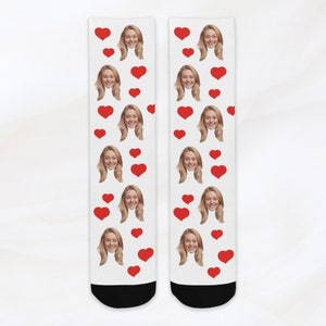 May include: A pair of white socks with a repeating pattern of red hearts and a woman's face.