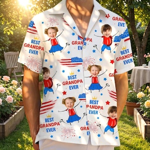 May include: White button-down shirt with a repeating pattern of children, fireworks, American flags, and the text "Best Grandpa Ever." The shirt has a classic collar and short sleeves, perfect for a summer day.