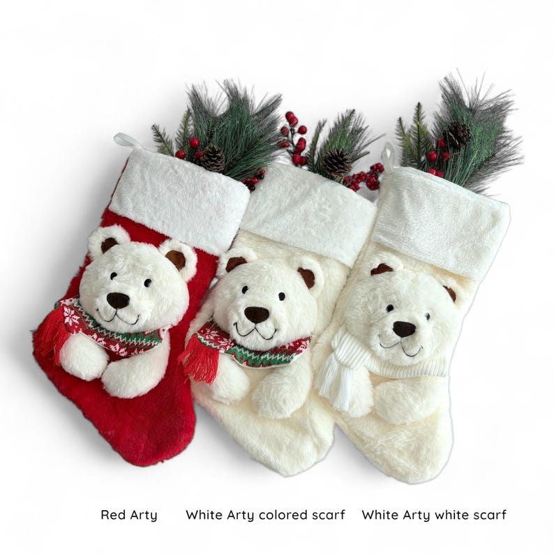 May include: Three Christmas stockings with polar bear faces. One stocking is red, and the other two are white. Each bear wears a scarf. The stockings are decorated with faux pine and berries.