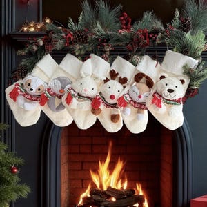 May include: Six festive Christmas stockings, each adorned with a different soft toy animal wearing a red and green scarf. The white stockings hang above a fireplace decorated with festive greenery and lights, creating a warm holiday atmosphere.