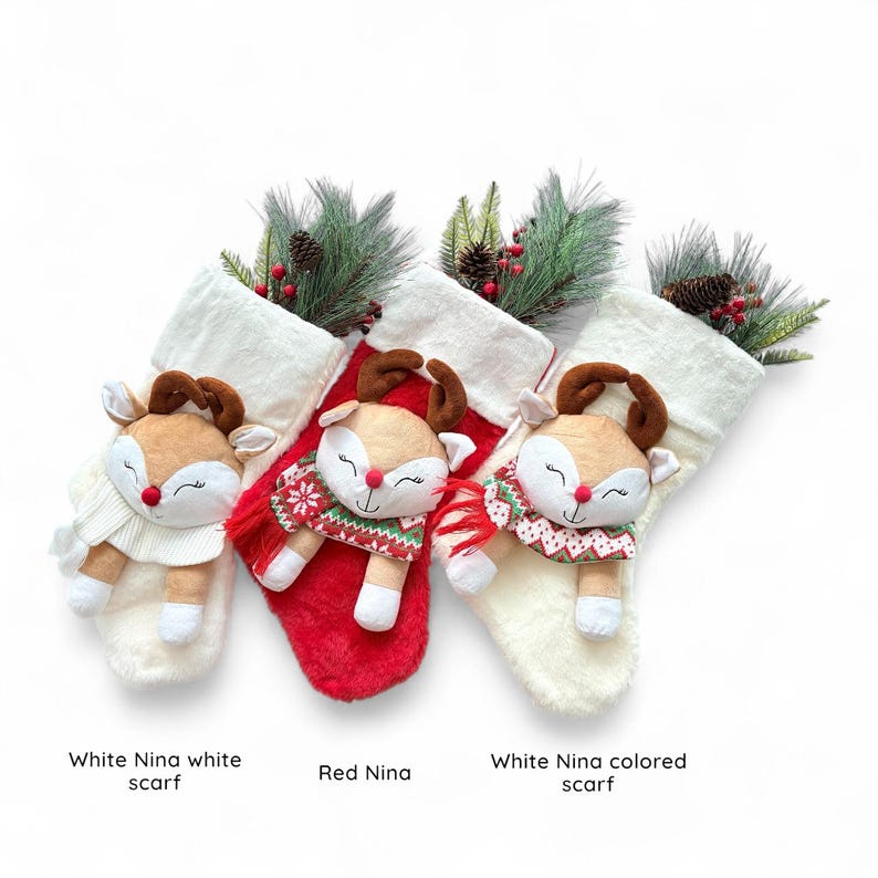 May include: Three Christmas stockings featuring reindeer plushies. The stockings are white and red, with faux fur trim. Each reindeer has brown antlers, a red nose, and a scarf. The stockings are decorated with pine and berries. Text on the image reads "White Nina white scarf", "Red Nina", and "White Nina colored scarf".