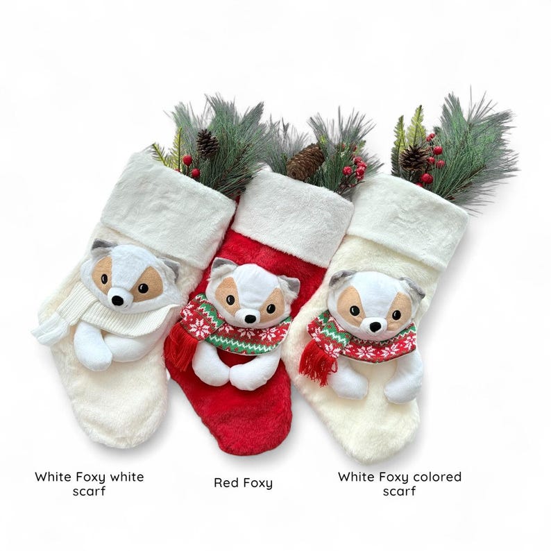 May include: Three Christmas stockings with fox ornaments. One stocking is red, and two are white. Each fox wears a scarf. The stockings are decorated with pine and berries.