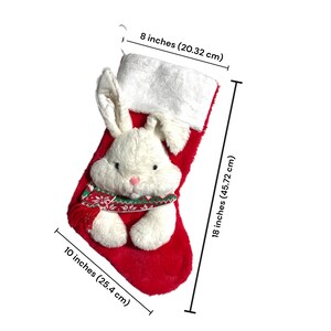 May include: A festive red Christmas stocking featuring a white plush bunny face and ears. The stocking measures 45.72 cm long and 25.4 cm wide, with a white cuff and a decorative scarf. The stocking is 20.32 cm wide.