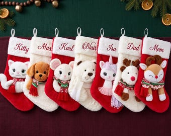 Op de afbeelding: Zeven kerstsokken met witte randen van imitatiebont, geborduurd met de namen Kitty, Max, Karl, Blair, Isa, Dad en Mom. Elke sok is voorzien van een pluche dierenfiguur, waaronder een kat, hond, muis, beer, eenhoorn, rendier en hert.
