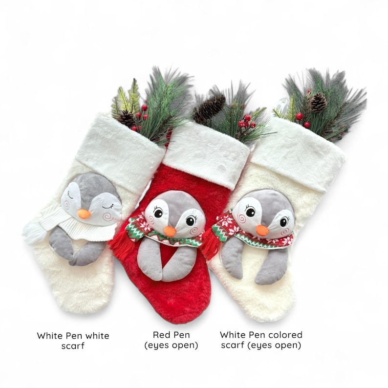 May include: Three Christmas stockings featuring penguin designs. One is red, and two are white. Each stocking has a plush penguin face and is decorated with greenery and pine cones. The text at the bottom reads "White Pen white scarf", "Red Pen (eyes open)", and "White Pen colored scarf (eyes open)".