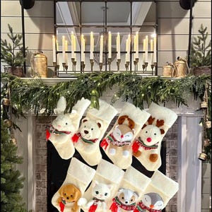 May include: A display of cream Christmas stockings, each featuring a plush animal character such as a rabbit, bear, fox, and reindeer. The stockings are arranged on a fireplace mantel decorated with greenery and candles, creating a festive holiday scene.