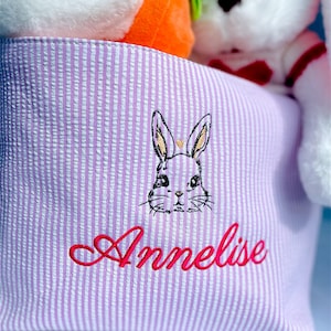 May include: A purple and white striped fabric storage bin with a bunny embroidered on the front. The bin is personalized with the name "Annelise" in pink thread.