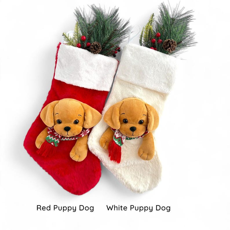 May include: Two Christmas stockings, one red and one cream, each featuring a plush puppy dog. The dogs wear festive scarves and are set against a white background. The stockings are decorated with greenery.