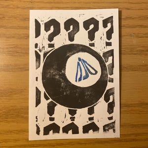 May include: A black and white print featuring a large black eight ball with a blue design inside a white circle. Question marks surround the eight ball and at the bottom. The print is on a white rectangular card.