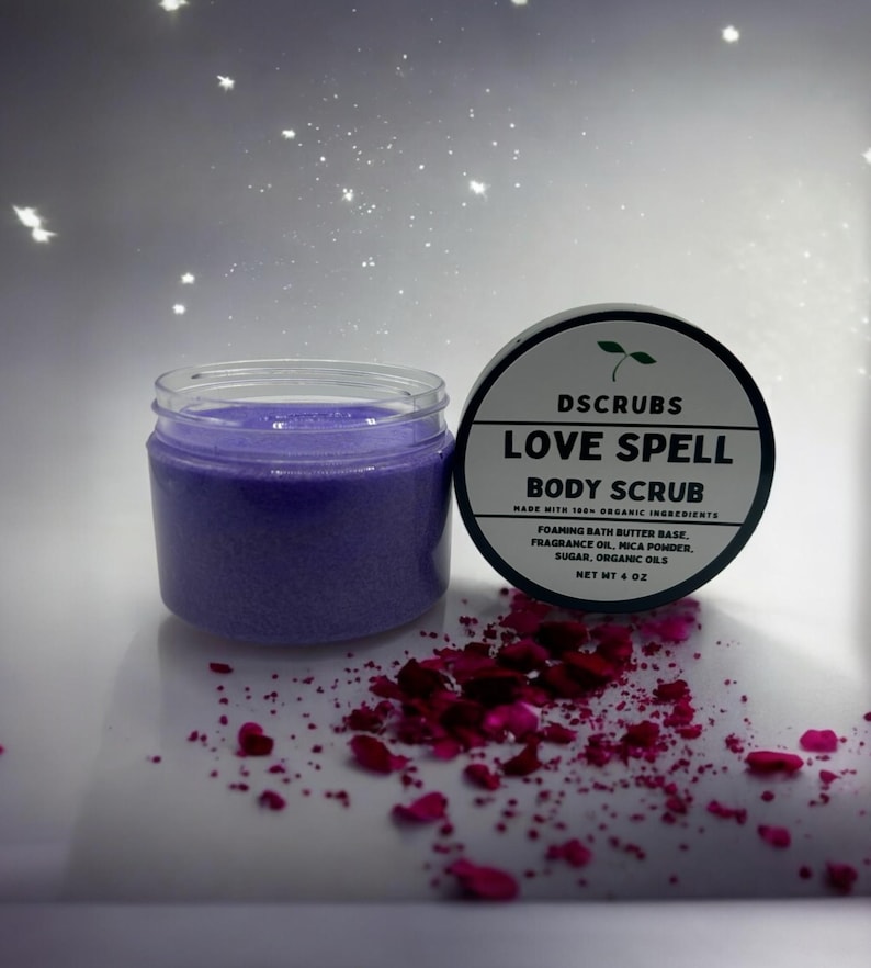 May include: A purple body scrub jar with a black lid and white text that reads "DSCRUBS LOVE SPELL BODY SCRUB MADE WITH 100% ORGANIC INGREDIENTS FOAMING BATH BUTTER BASE, FRAGRANCE OIL, MICA POWDER, SUGAR, ORGANIC OILS NET WT 4 OZ".