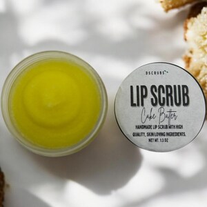 Puede incluir: Un peque&ntilde;o tarro de exfoliante labial amarillo con una etiqueta blanca que dice "DSCRUBS LIP SCRUB Cake Batter HANDMADE LIP SCRUB WITH HIGH QUALITY, SKIN LOVING INGREDIENTS. NET WT. 1.3 OZ"